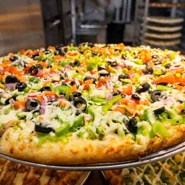 Large vegetarian pizza with black olives, green peppers, red onions, and tomatoes on a metal tray.