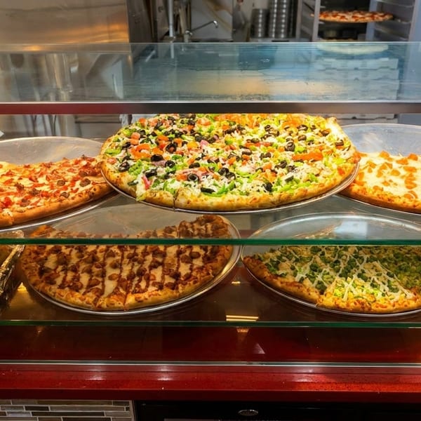 A glass display case filled with various pizzas, including pepperoni, vegetable, and plain cheese.